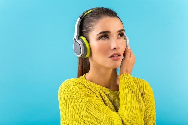 Atractiva mujer joven con estilo escuchando música en auriculares inalámbricos feliz vistiendo suéter de punto amarillo estilo colorido moda posando