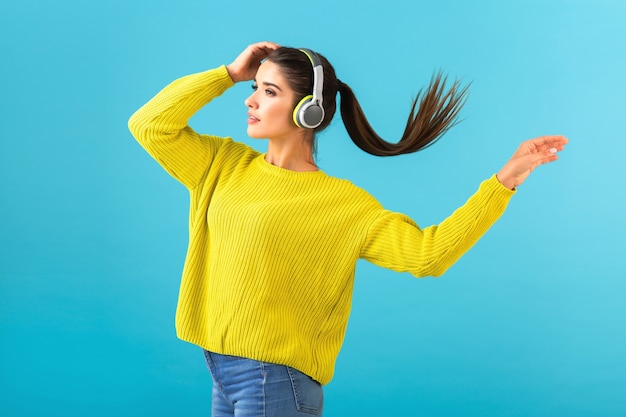 Atractiva mujer joven con estilo escuchando música en auriculares inalámbricos feliz vistiendo suéter de punto amarillo