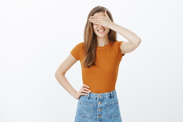 Atractiva mujer joven con estilo esperando sorpresa, cubrirse los ojos y sonriendo, anticipando