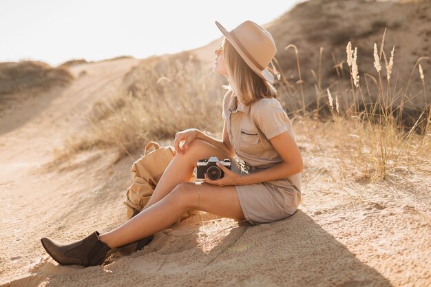 Atractiva mujer joven con estilo en vestido caqui en el desierto, viajando en África en un safari, con sombrero y mochila