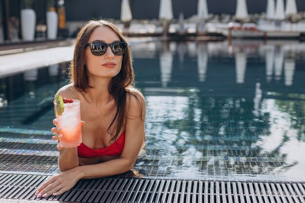 Atractiva mujer joven junto a la piscina bebiendo cócteles