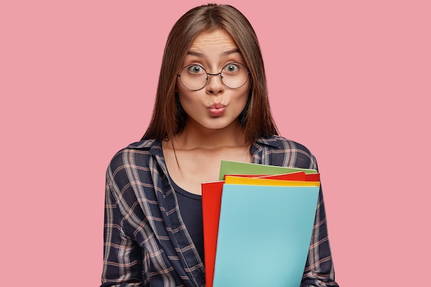 Atractiva mujer joven posando contra la pared rosa con gafas