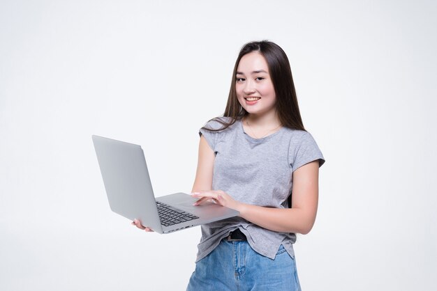 Atractiva mujer joven sonriente sosteniendo el ordenador portátil aislado en la pared blanca