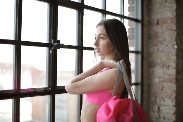 Atractiva mujer joven en un traje de gimnasio sosteniendo su bolso y mirando por la ventana