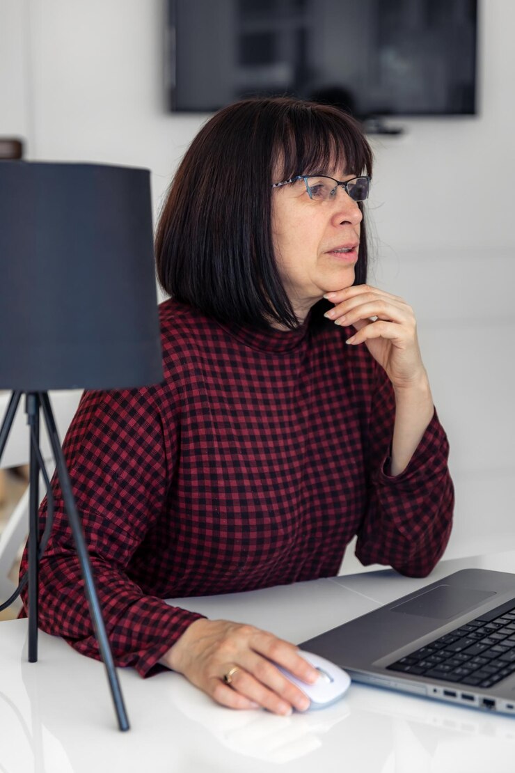 Foto gratuito atractiva mujer de mediana edad que trabaja en una computadora portátil mientras está sentada en una mesa