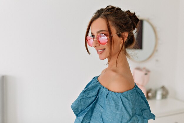 Atractiva mujer morena con estilo con el pelo recogido con gafas de color rosa y top azul