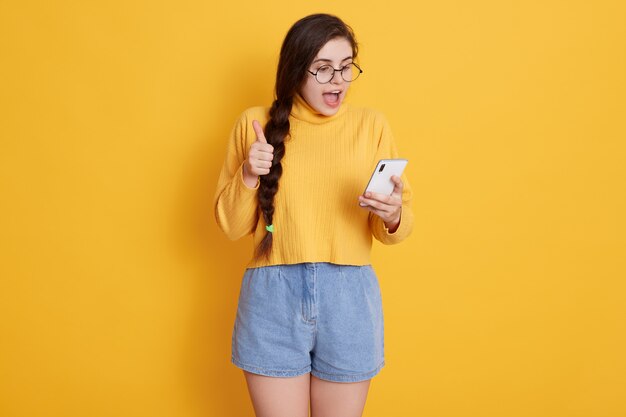 Atractiva mujer morena gritando algo feliz mientras mira el teléfono inteligente en sus manos