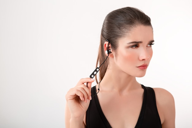 Foto gratuita atractiva mujer morena en jogging top negro escuchando música en auriculares posando