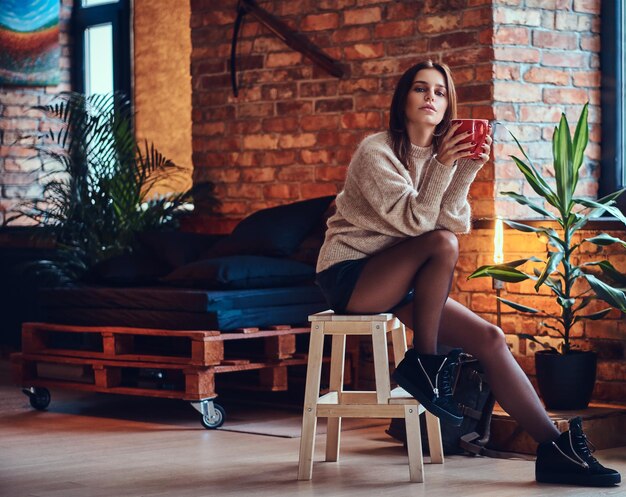 Atractiva mujer morena posando cerca de la ventana en una habitación con interior tipo loft.