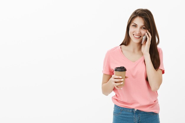 Atractiva mujer morena posando en el estudio con su teléfono y café