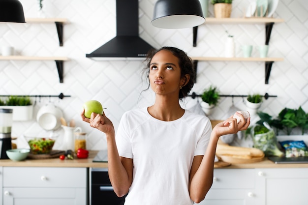 La atractiva mujer mulata sonrió pensando en una manzana con cara hilarante y mirando hacia la parte superior de la moderna cocina blanca