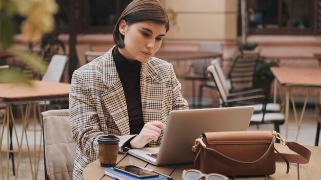 Atractiva mujer de negocios que parece segura de resolver problemas de trabajo en una computadora portátil que trabaja durante el descanso para tomar café en un acogedor café al aire libre Tecnología moderna