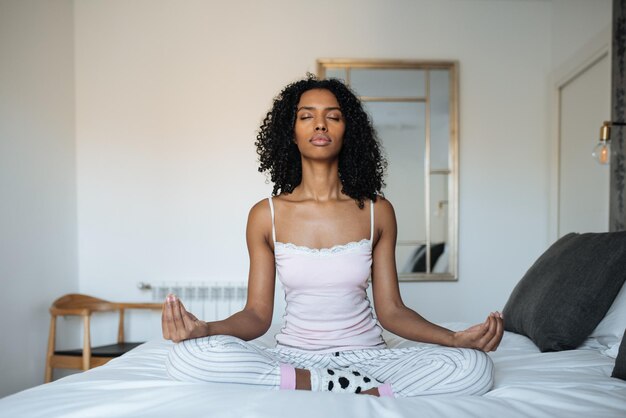 Atractiva mujer negra en cama meditando