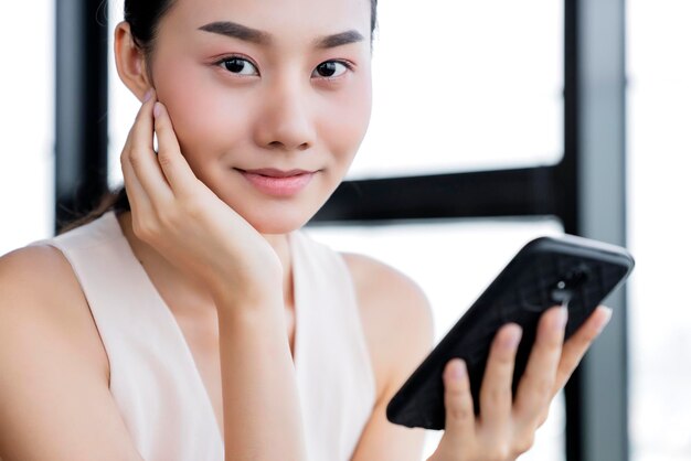 Atractiva mujer de oficina asiática felicidad y comunicación alegre con el cliente en el fondo de la oficina del teléfono inteligente