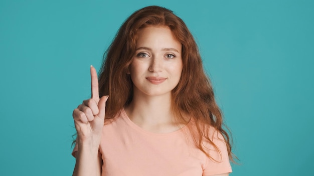 Atractiva mujer pelirroja mostrando el dedo índice en la cámara sobre un fondo colorido