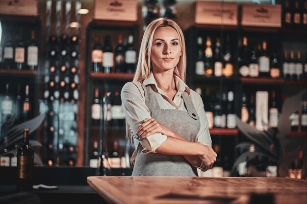 Atractiva mujer pensativa en uniforme está esperando a los clientes en su restaurante de vinos.