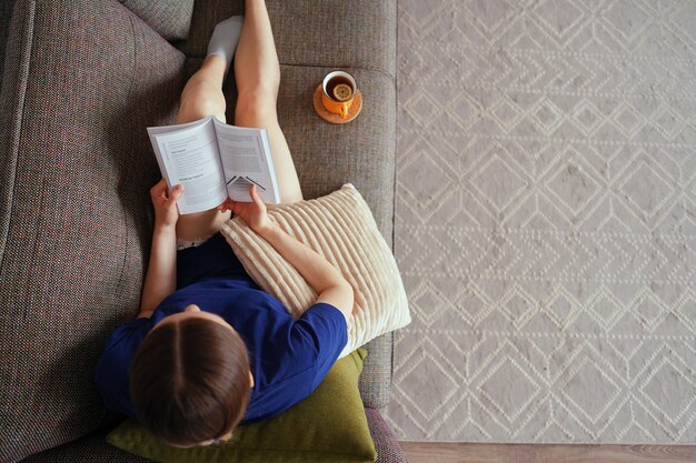 Atractiva mujer positiva leyendo un libro descansando en el sofá