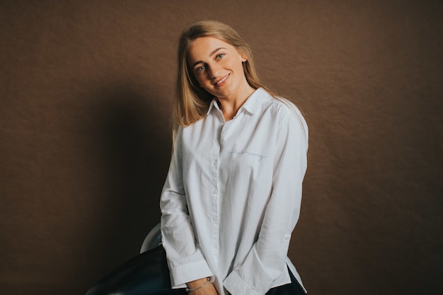 Atractiva mujer rubia caucásica con una camisa blanca posando sobre un fondo marrón