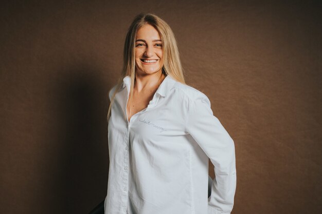 Una atractiva mujer rubia caucásica con una camisa blanca posando sobre un fondo marrón