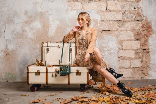 Atractiva mujer rubia con estilo en abrigo beige caminando en la calle contra la pared vintage