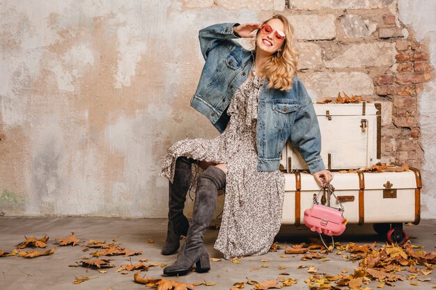 Atractiva mujer rubia con estilo en jeans y chaqueta de gran tamaño caminando contra la pared en la calle