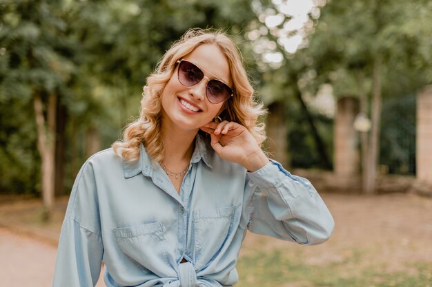 Atractiva mujer rubia sonriente caminando en el parque en traje elegante