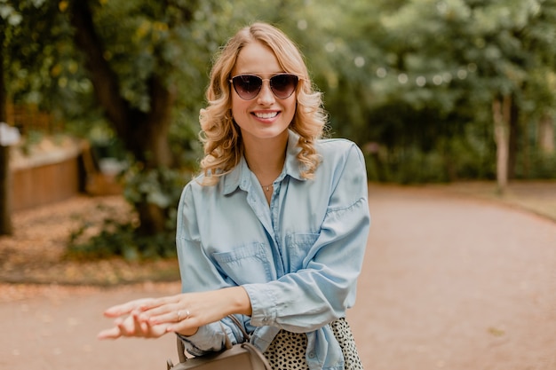 Atractiva mujer rubia sonriente caminando en el parque en traje elegante