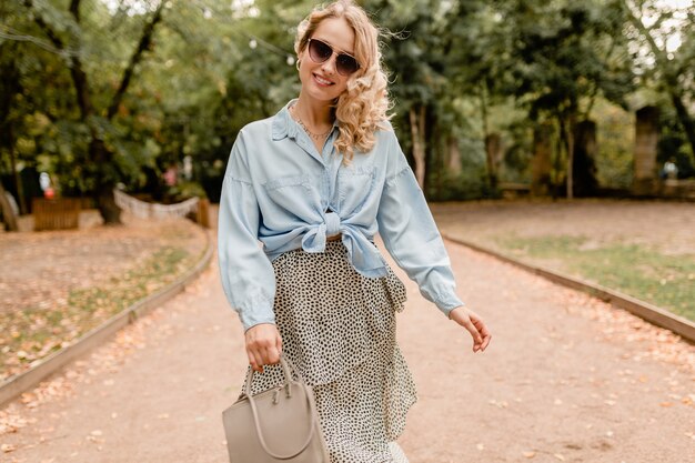 Atractiva mujer rubia sonriente caminando en el parque en traje de verano