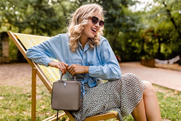 Atractiva mujer rubia sonriente sentada en la tumbona en traje de verano