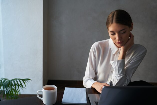 Atractiva mujer sentada a la mesa y trabajando en equipo portátil