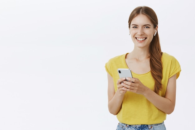 Atractiva mujer sonriente en auriculares escuchando música o podcast, con smartphone