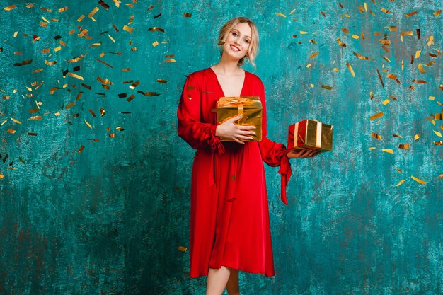 Atractiva mujer sonriente feliz con elegante vestido rojo celebrando la Navidad y el año nuevo con regalos
