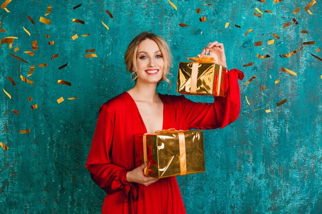 Atractiva mujer sonriente feliz con elegante vestido rojo celebrando la Navidad y el año nuevo con regalos