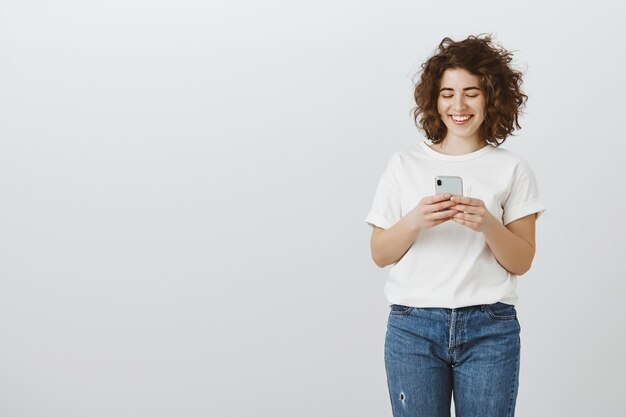 Atractiva mujer sonriente mediante teléfono móvil, mensajes de texto, redes sociales de desplazamiento