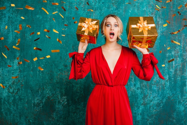 Atractiva mujer sorprendida en elegante vestido rojo celebrando la Navidad y el año nuevo con regalos