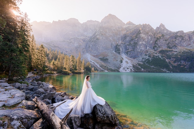 Atractiva novia está de pie cerca del lago Highland con pintorescas vistas de las montañas de otoño