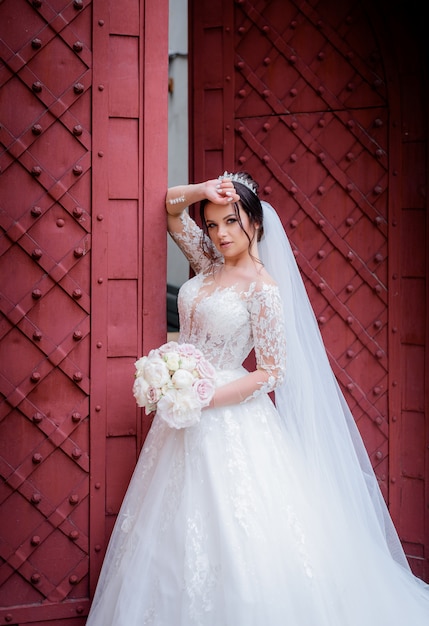 Atractiva novia vestida con un vestido de lujo cerca de la entrada roja