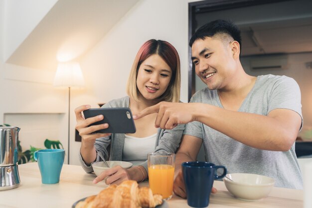 Atractiva pareja asiática joven distraída en la mesa con periódico y teléfono celular