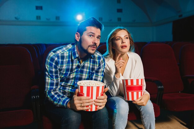 Atractiva pareja caucásica joven viendo una película en una sala de cine, una casa o un cine. Luce expresivo, asombrado y emocionado. Sentarse solo y divertirse. Relación, amor, familia, fin de semana.