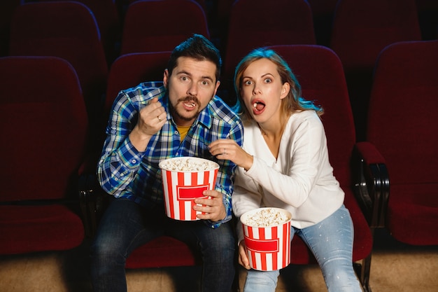 Atractiva pareja caucásica joven viendo una película en una sala de cine, una casa o un cine. Luce expresivo, asombrado y emocionado. Sentarse solo y divertirse. Relación, amor, familia, fin de semana.