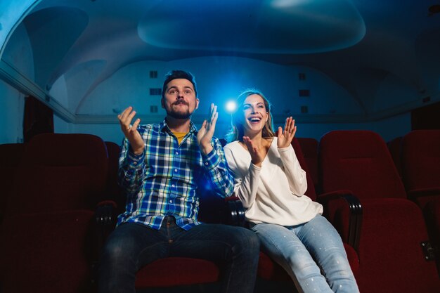 Atractiva pareja caucásica joven viendo una película en una sala de cine, una casa o un cine. Luce expresivo, asombrado y emocionado. Sentarse solo y divertirse. Relación, amor, familia, fin de semana.