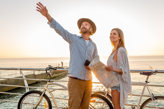 Atractiva pareja feliz viajando en verano en bicicleta, hombre y mujer con cabello rubio boho hipster estilo moda divirtiéndose juntos