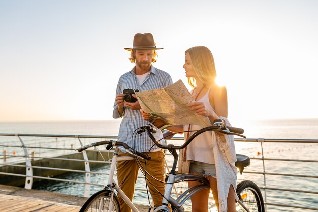 Atractiva pareja feliz viajando en verano en bicicleta, hombre y mujer con cabello rubio boho hipster estilo moda divirtiéndose juntos