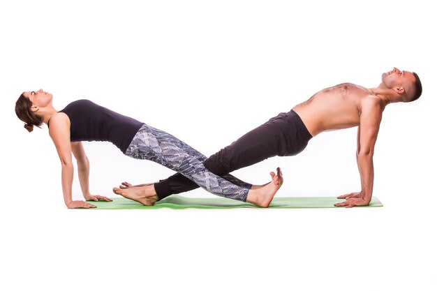 Atractiva pareja haciendo yoga juntos sobre fondo blanco.