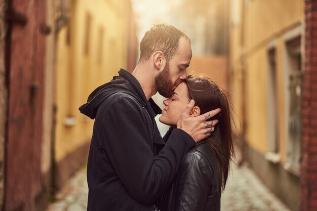 Atractiva pareja, hombre barbudo y chica morena besándose fuera de la vieja calle europea sobre un fondo.