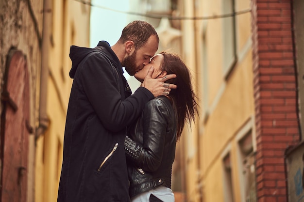 Atractiva pareja, hombre barbudo y chica morena besándose fuera de la vieja calle europea sobre un fondo.