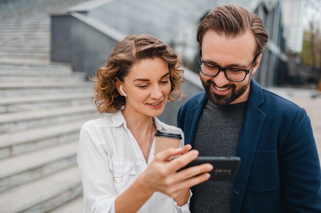 Atractiva pareja de hombre y mujer en el centro urbano de la ciudad, sosteniendo el teléfono y mirando