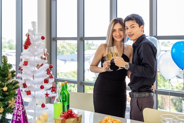 Atractiva pareja joven celebra la Navidad y el Año Nuevo en una copa de champán con bocadillos y bebidas en la mesa