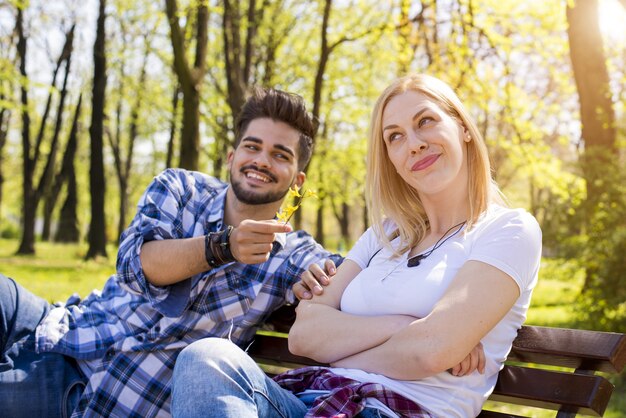 Atractiva pareja joven coqueteando y divirtiéndose en un banco del parque