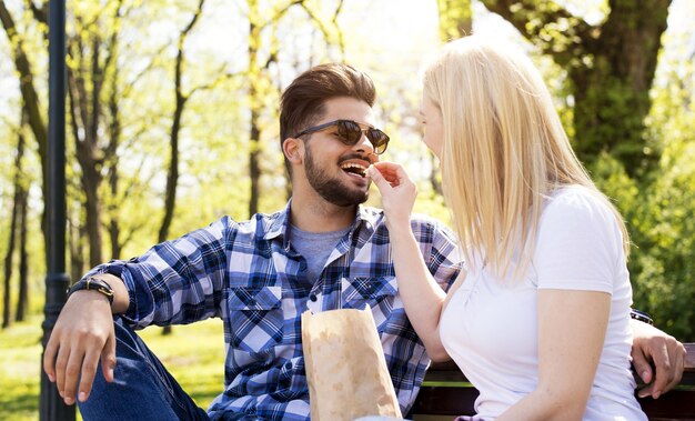 Atractiva pareja joven divirtiéndose y comiendo palomitas de maíz en un banco del parque